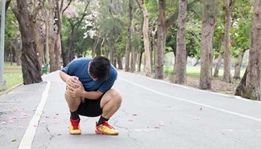Runner crouched holding knee on running path